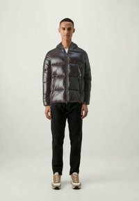 Polstret, skinnende mørkegrå dunjakke med hætte, frontlynlås og sidelommer. Sammen med sorte bukser og lysebrune sneakers.