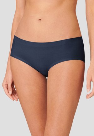 Woman wearing seamless dark navy hipster-style underwear, showing midriff and upper thighs against plain light background.