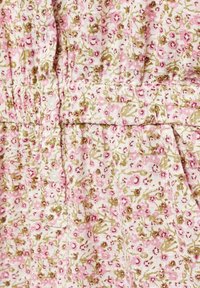 Tkanina s květinovým vzorem zobrazuje růžové a zelené květiny na bílém pozadí. Nařasené detaily s malými bílými knoflíky.