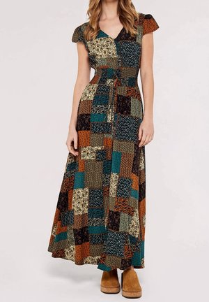 Kobieta ubrana w maxi sukienkę patchwork z dekoltem w serek, krótkimi rękawkami typu cap i wiązaniem w talii, w połączeniu z brązowymi zamszowymi botkami za kostkę.