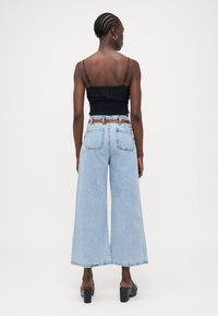 Jeans de perna larga azul-claro com bainha desenhada, combinados com um top crop preto franzido. O conjunto inclui um cinto castanho e sapatos de salto grossos pretos.