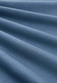 Miękka niebieska tkanina z gładkimi, delikatnymi fałdami tworzącymi subtelne cienie i fakturę.