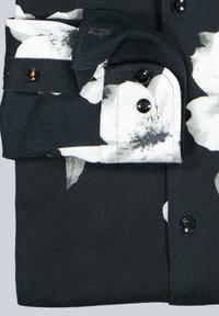 Schwarzes Hemd mit weißem Blumenmuster, Knöpfen an den Manschetten und dunklen Knöpfen. Der Stoff scheint weich mit einer glatten Textur zu sein.