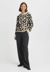 Pull en imprimé léopard beige avec un col rond, associé à un pantalon large gris. Le pull présente des taches noires et des poignets côtelés.
