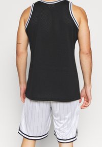 Débardeur en maille noire avec un col rond et des accents blancs, associé à un short blanc à fines rayures avec des bordures noires et des poches latérales.