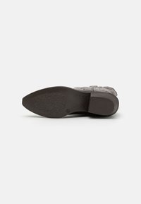 Suela de zapato marrón con un patrón, con forma puntiaguda, superficie texturizada y un ligero tacón. Incluye un logotipo impreso cerca del área del tacón.
