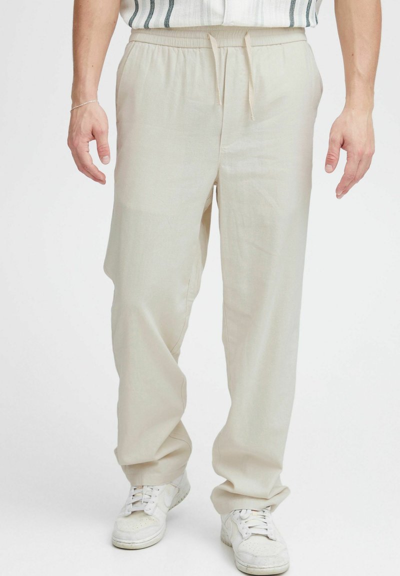Hellbeige, locker sitzende Hosen mit elastischem Bund und Kordelzug. Hergestellt aus einem glatten Stoff, mit seitlichen Taschen und geripptem Muster.