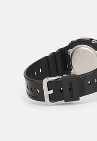 Black rubber watch strap with a silver metal buckle and a stainless steel back. Features multiple holes for adjustable fit.