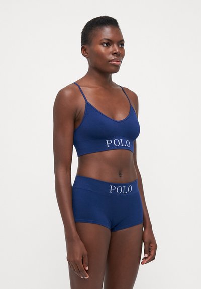 Marineblauwe geribbelde bralette en hipster shorts set met logo tailleband, voorzien van verstelbare bandjes en naadloos ontwerp. Zachte textuur.