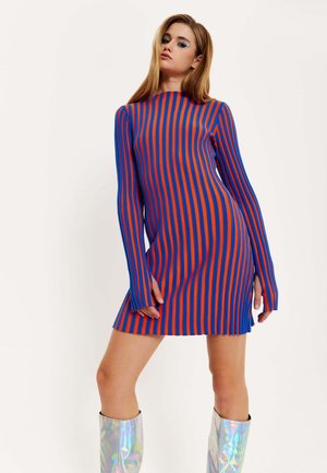 Striped knit dress in blue and red, with long sleeves and side slits. Model wearing metallic knee-high boots. Smooth texture, fitted design.