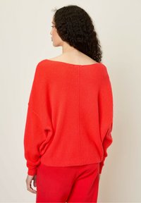 Rød strikket sweater med en bred halsudskæring og let sænkede skuldre, med ribbede manchetter og kant, vist fra ryggen.