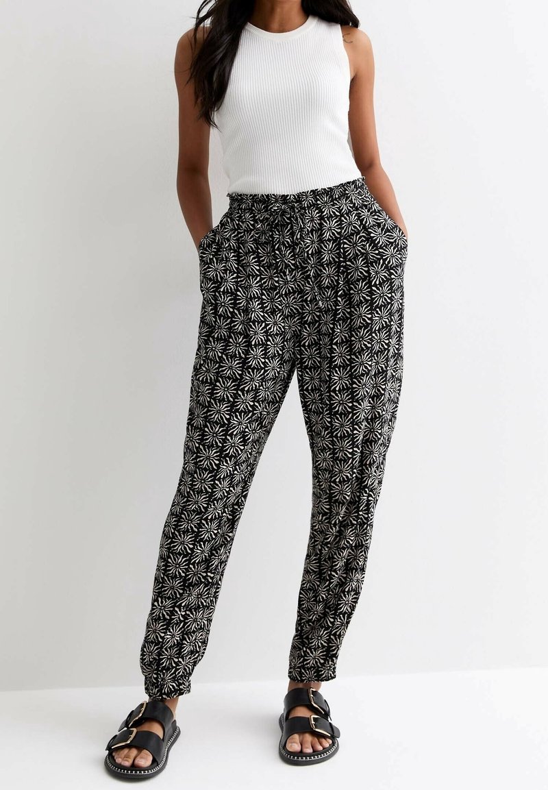 Pantalons à motifs noir et blanc avec une taille élastique, poches latérales et chevilles resserrées, associés à un haut sans manches blanc ajusté.