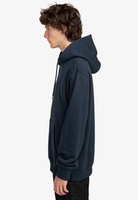 Marineblauwe pullover hoodie gemaakt van zacht katoen, voorzien van een frontzak, trekkoorden in de capuchon en ribgebreide manchetten. Casual pasvorm en gladde textuur.