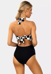 Czarny i biały kostium kąpielowy w kratę z halterem, związany z tyłu, w połączeniu z czarnymi majteczkami z wysokim stanem. Gładka faktura.
