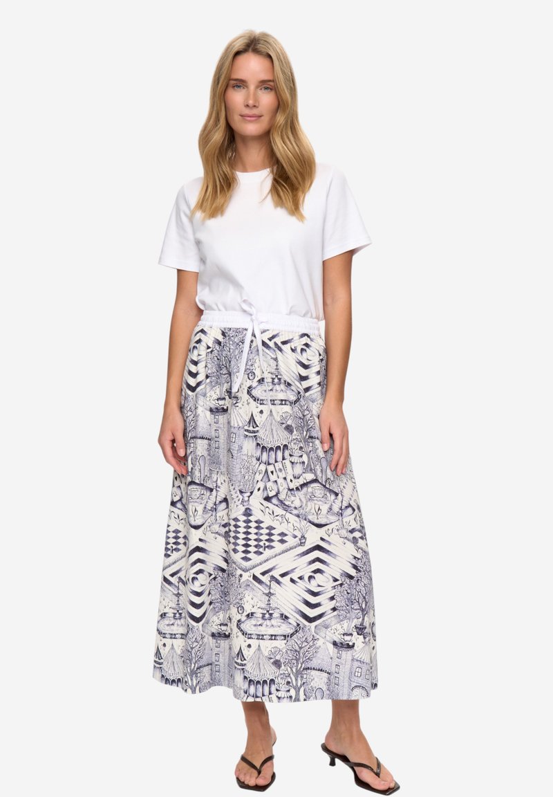 Jupe longue avec une taille élastique blanche à cordon, arborant un motif complexe bleu et blanc de paysages et de formes géométriques. Associée à un t-shirt blanc uni.