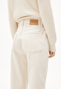 Krämbelägen högmidjade jeans med en avslappnad passform, med bakfickor och en brun läderetikett med "ARMEDANGELS" präglat i guld.