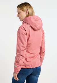 Ljusrosa huvjacka gjord av texturerat tyg, med elastiska ärmslut och en figursydd design, som bärs över mörkblå jeans.