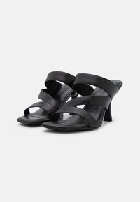 Sandalias negras de tacón con múltiples correas anchas, diseño de punta abierta y forma de punta cuadrada con un tacón acampanado. Textura de cuero suave.