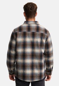 Camicia a quadri marrone, blu e crema con vestibilità comoda, collo con bottoni, tessuto strutturato, cuciture visibili e polsini con bottoni.