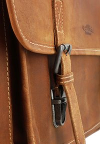 Brun læder messenger taske med en struktureret overflade, synlige syninger og en metalspænde til lukning. Ren, minimalistisk design.