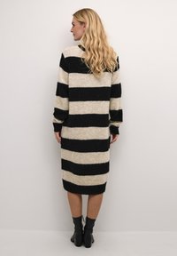 Robe pull longue en tricot avec des rayures alternées noires et beiges, coupe décontractée, poignets côtelés et longueur mi-mollet.