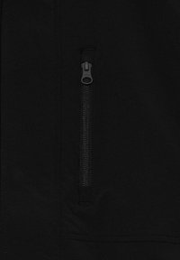 Detailní záběr na látku černé bundy s viditelnou kapsou na zip, ukazující hladkou texturu a precizní detaily šití.