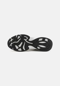 Sorte svart-hvitt sportsko såle med teksturerte gummimønstre, med hevede områder for grep og støtte. Holdbare materialer er brukt.