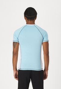 Ανοιχτό μπλε αθλητικό μπλουζάκι με κοντά μανίκια, λευκές πλευρικές πάντες και αντίθετες γκρι ραφές. Λείο ύφασμα, εφαρμοστή γραμμή.