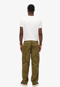 Olijfgroene cargobroek met meerdere zijzakken en een elastische tailleband, samen met een eenvoudige witte t-shirt met korte mouwen.