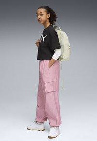 Black cropped t-shirt with white Puma logo, pink cargo pants with pockets, white sneakers, and a light green backpack.
