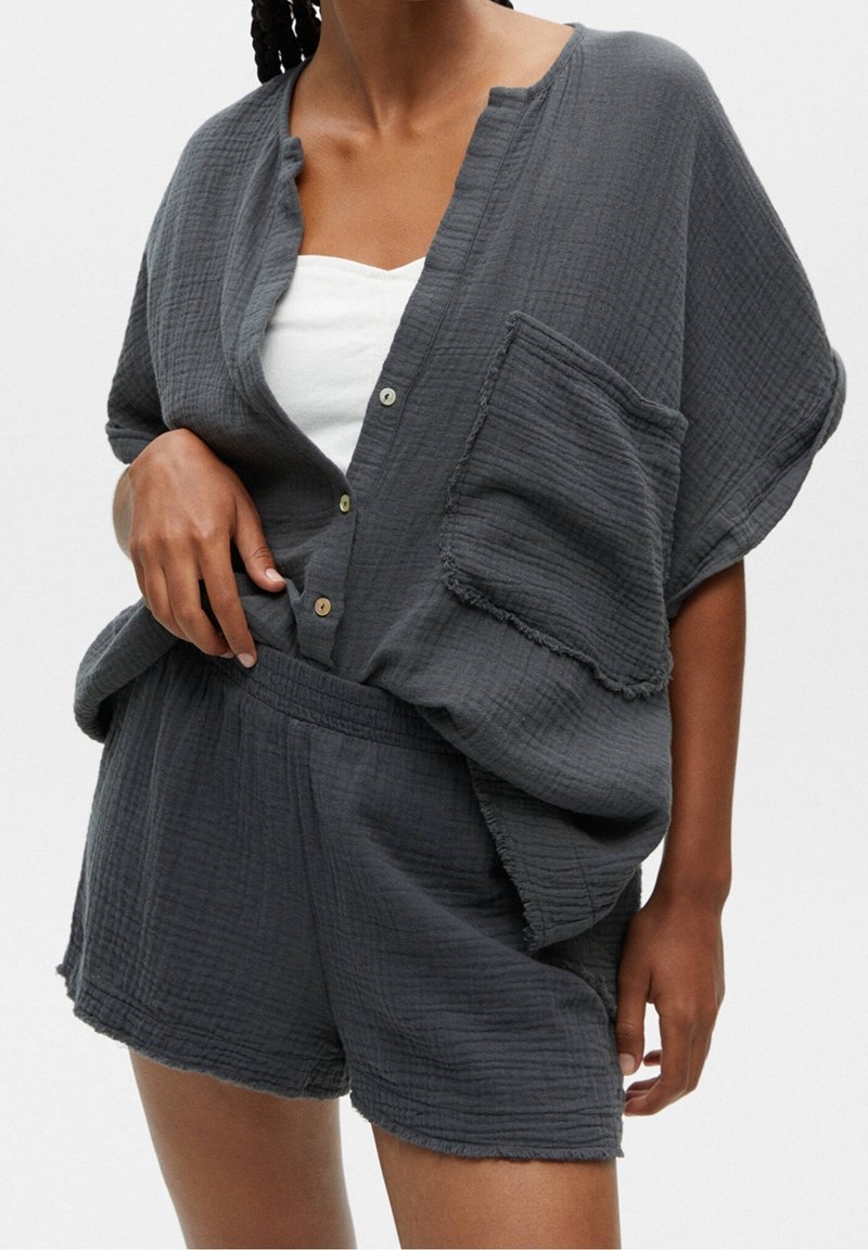 Chemise grise texturée à boutons avec une poche frontale, associée à un short assorti. Les deux pièces ont une coupe ample et des bords effilochés.