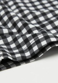 Černobílá kostkovaná tkanina s hladkým povrchem. Má zakřivený okraj a pečlivě prošitý lem podél spodní části.