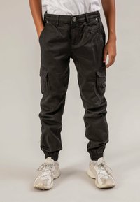 Pantalon cargo noir avec poignets élastiques, multiples poches et coupe ample, fabriqué en tissu durable, porté avec des baskets blanches.