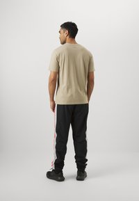 Beige cotton t-shirt with short sleeves, paired with black track pants featuring red and grey side stripes. Simple design, athletic fit.