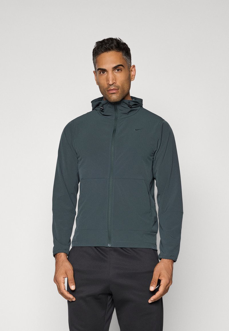 Nike hættejakke i mørkegrøn med frontlynlås, to lommer og justerbare snore. Blødt, letvægtsstof og tætsiddende design.
