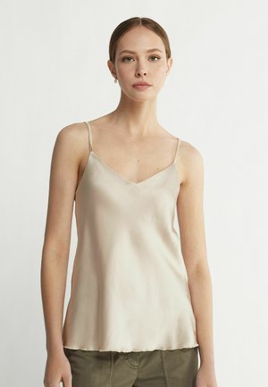 Camisole en satin beige clair avec un décolleté en V et des bretelles fines. Texture douce et coupe ample, tombant juste au-dessus de la taille.