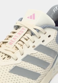 Pantofii sport bej cu partea superioară din plasă, accente gri, trei dungi gri și eticheta roz "HEAT.RDY"; dispun de un sistem de șireturi reglabil.