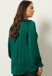 Grüne Bluse aus glattem, strukturiertem Stoff, mit Puffärmeln und rüschierten Bündchen. Das Design hat eine lockere Passform und einen abgerundeten Saum.