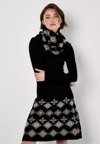 Abito di maglia nero con maniche lunghe, caratterizzato da una gonna a fantasia bianco e nero con motivi a diamante. Accentuato da una sciarpa infinity abbinata in nero e bianco.