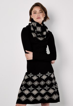 Robe tricot noire à manches longues, dotée d'une jupe à motifs noir et blanc avec des motifs en losanges. Accentuée d'une écharpe en infini assortie noir et blanc.