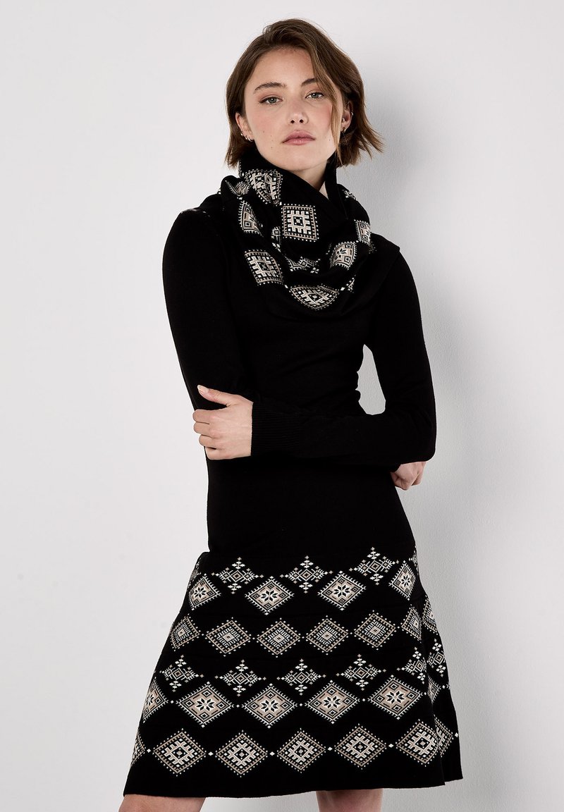 Abito di maglia nero con maniche lunghe, caratterizzato da una gonna a fantasia bianco e nero con motivi a diamante. Accentuato da una sciarpa infinity abbinata in nero e bianco.