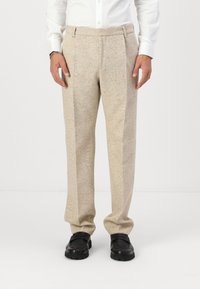 Beige wool trousers with a textured finish, featuring a tailored fit, pleated front, and straight legs, paired with black slip-on shoes.