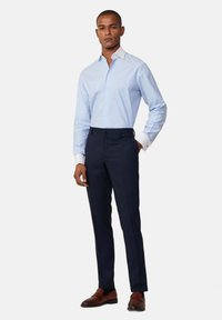 Lichtblauw gestreept overhemd met witte kraag, gecombineerd met donkerblauwe broek en bruine leren instappers, staande op een effen achtergrond.