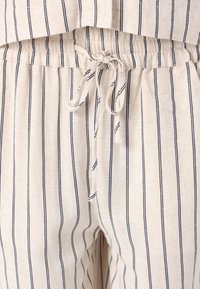 Pantalons en mélange de lin avec un fond beige clair et des rayures horizontales bleu marine. Présentent une taille élastique et un cordon de serrage.