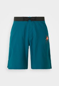 Turquoise swim shorts made of lightweight material. Features a black elastic waistband with drawstring and an orange logo on the left side.