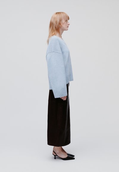 Light blue knitted sweater with ribbed cuffs paired with a long black skirt and pointed black heels. Minimalist design, smooth texture.
