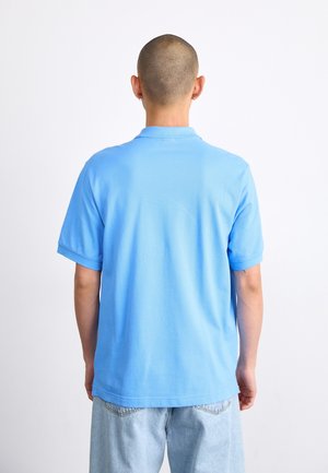 Polo bleu clair en coton, avec un col classique, des manches courtes et une coupe décontractée. Porté avec un jean en denim clair.