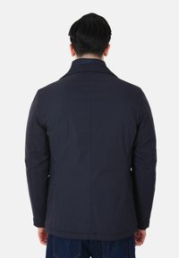 Giacca blu navy in tessuto liscio, con colletto, due tasche laterali e vestibilità sagomata, con design posteriore semplice.