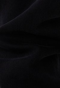 Tejido negro de punto con una textura suave, que muestra pliegues y sutiles variaciones en el tono. Acabado uniforme y liso sin patrones.