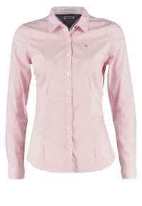 Chemisier pour femmes cintré avec des rayures verticales rouges et blanches, manches longues, et un petit logo brodé sur la poitrine.